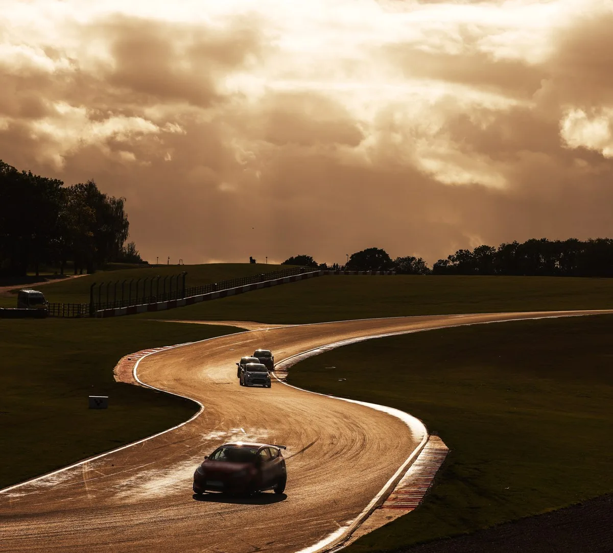 A racing car on a winding circuit under a dramatic evening sky