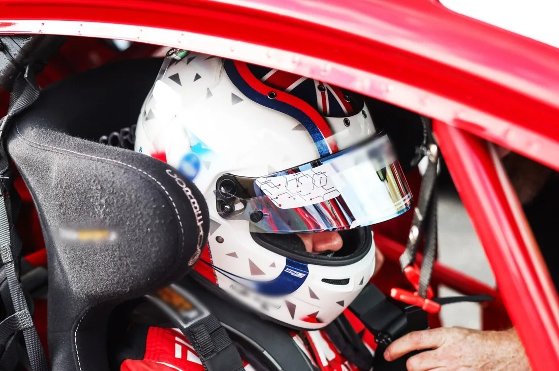 A driver in a white helmet strapped into a race car
